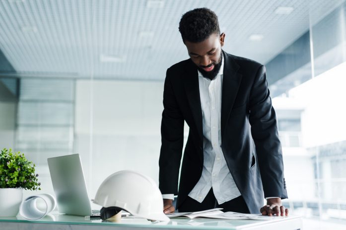 Successful businessman. Handsome young African man keeping arms crossed and looking at camera while standing in creative office